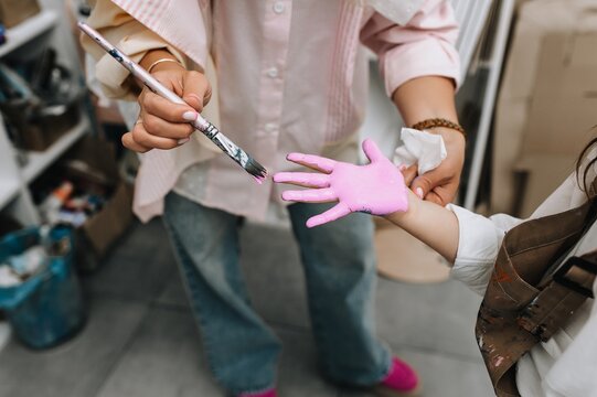 A professional artist paints a woman's hand with a brush and pink watercolors to create a handprint. Art concept.
