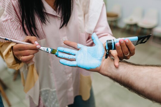 An artist paints a man's hand with a brush and colors it with blue watercolor paints.