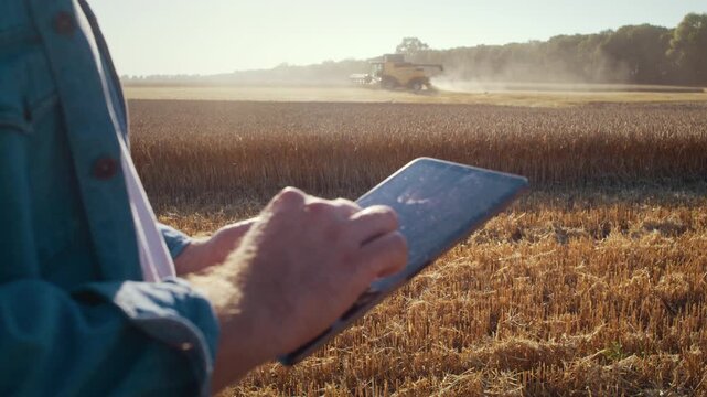Agronomist controls harvesting via tablet as reaper cuts wheat