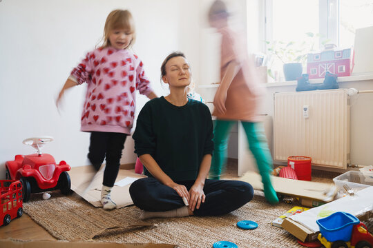 Stressed out mother sitting on floor while children running around her.
