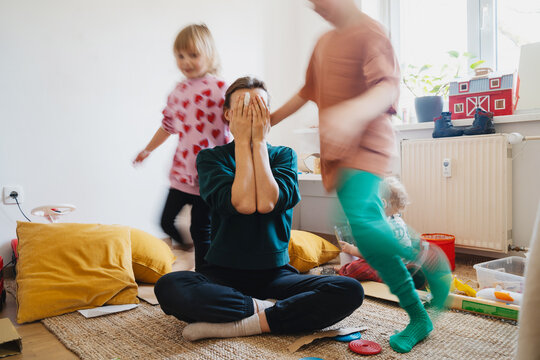 Stressed out mother sitting on floor while children running around her.