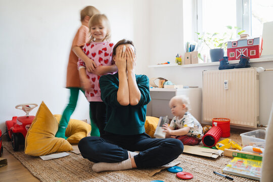 Stressed out mother sitting on floor while children running around her.