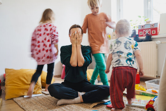 Stressed out mother sitting on floor while children running around her.