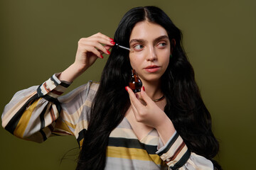 Young woman with long hair applies beauty product on her face while wearing a striped blouse