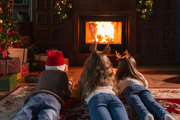 Merry Christmas Xmas holiday. Children lying down resting playing having fun near fireplace. Happy kids playing in living room with Christmas tree and fireplace. Christmas eve at home © Юлия Завалишина