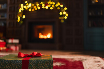 Naklejka premium Green gift box in classical Christmas decorated interior living room library with fireplace. Christmas gift near fir tree on Christmas eve. Modern classic style interior design apartment. Christmas
