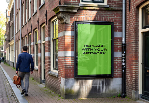 Vertical poster mockup displayed on a brick building exterior in an urban street scene, pedestrian walking past, realistic outdoor signage presentation with screen placeholder