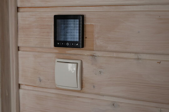 Smart digital thermostat and light switch on wooden wall. Modern digital smart thermostat and light switch on wooden wall for indoor temperature control.