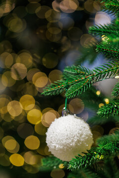 White Christmas ornament on fir tree with golden bokeh lights