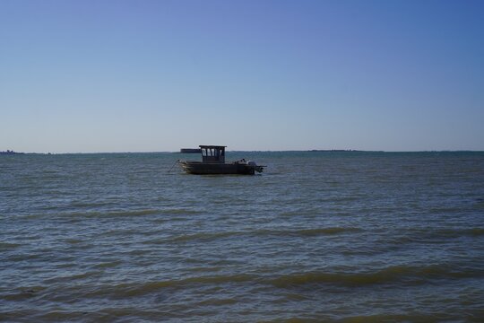 A small wooden workboat with a small cabin rests anchored in open coastal waters under a clear, bright sky. 