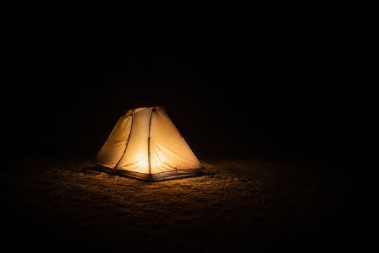 Warm light spilling from a lit tent onto dark ground