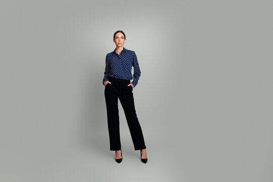 Business woman standing confidently in polka dot blouse and black trousers &mdash; professional full-length portrait on a neutral gray background, elegant corporate style and poised posture