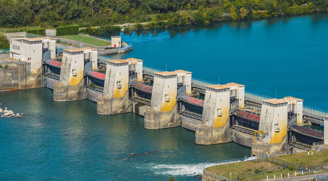 Aerial view of the hydroelectric dam on the Rhone River featuring concrete towers and spillway gates surrounded by a green landscape in Le Pouzin, Auvergne-Rhone-Alpes, France.