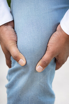 Hand closeup shot of South asian young adult man holding painful knee from accident or knee joint injury pain outdoor scene