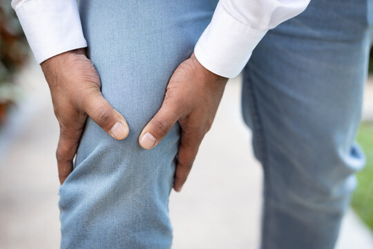 Hand closeup shot of South asian young adult man holding painful knee from accident or knee joint injury pain outdoor scene