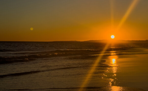 Sun touching the horizon line over calm ocean.
