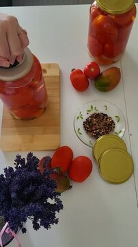 Using a manual capper to seal tomato jars in a home kitchen. traditional food storage, domestic preservation process, artisan skill.