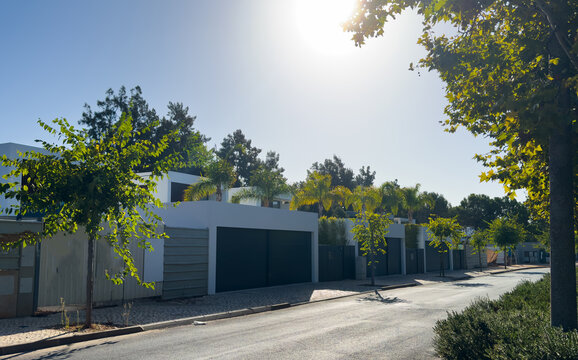 A contemporary minimalist residence with extensive glass windows offers a view of the lush green trees and manicured lawn, highlighting modern exterior design.