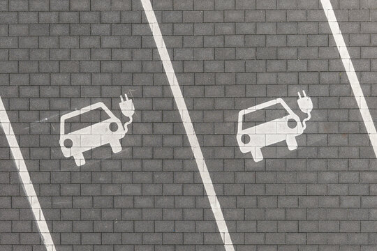 Aerial view of electric vehicle parking spaces with white painted car symbols and charging plugs on grey paved ground in Lincolnsiedlung, Darmstadt, Hessen, Germany.