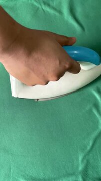 Close up of a woman's hand ironing a T-shirt at home in Dhaka, Bangladesh. Everyday household chore showcasing clothing care and a simple domestic routine.