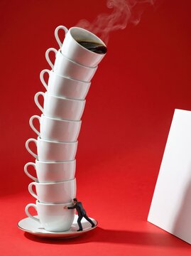 Miniature figure pushing stack of porcelain coffee cups against red backdrop