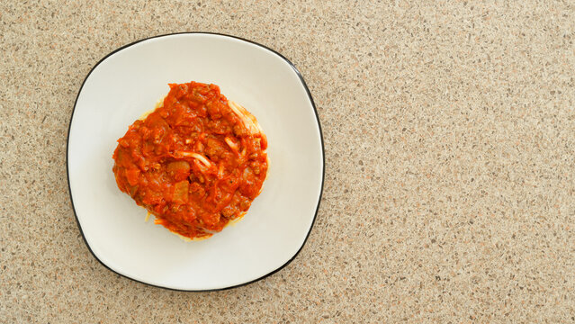 Overhead view of spaghetti topped with rich tomato meat sauce. served on a white plate.