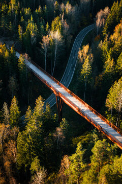 Aerial view of a wildlife bridge crossing over a winding road through a dense forest with autumn foliage in Sipoo, Uusimaa, Finland.