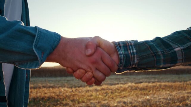 Male farmers handshake against back sunset field after agreement