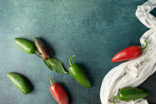 Green and red, jalapeno chili peppers on dark green background with a white cloth.