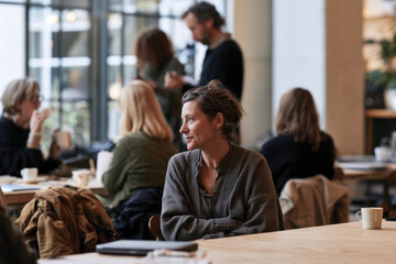 Fototapeta premium A woman is seated in a bright cafe, lost in thought while enjoying a coffee, symbolizing moments of tranquility and introspection amidst a lively social scene.