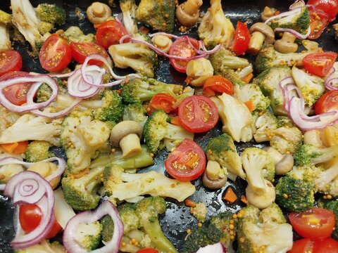 Colorful cooked vegetables with broccoli, mushrooms, cherry tomatoes and red onion on a pan, close-up healthy vegetarian meal background.