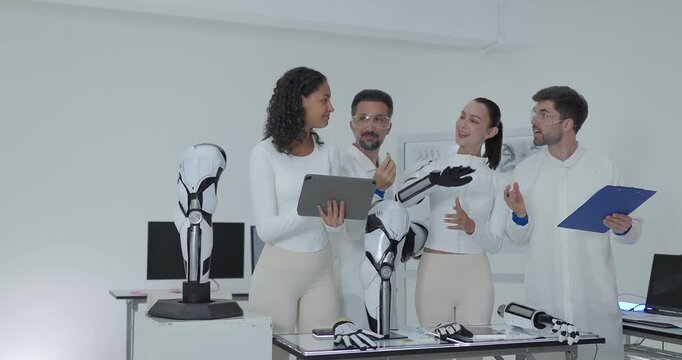 Robotics engineers inspecting robotic hand and arm standing together in bright white laboratory
