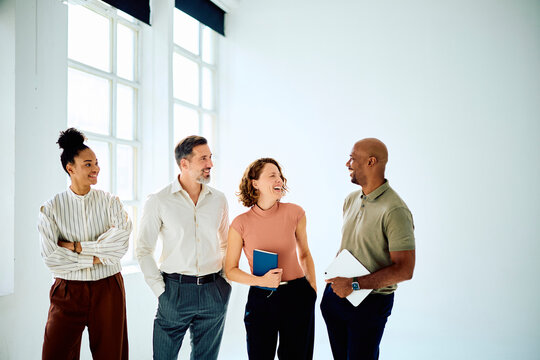 Diverse business colleagues networking, laughing, and sharing ideas in a bright office, representing teamwork and success