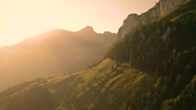 Aerial view of the Alpstein mountain range at sunset with golden light illuminating the grassy slopes and rocky peaks in Appenzell, Appenzell Innerrhoden, Switzerland.