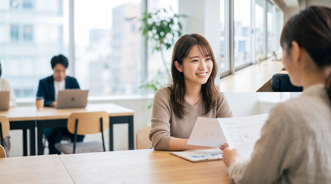 オフィスで書類を見ながら笑顔で打ち合わせをする女性会社員
