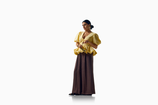 Fashionable woman models sculptural yellow blouse with flowing trousers. Concept of statement style, modern femininity, color contrast and expressive wardrobe.