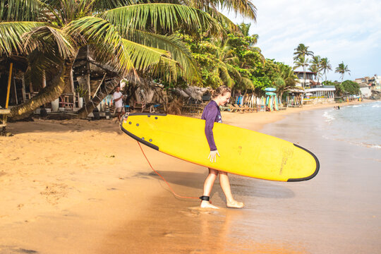 Young woman carrying yellow surfboard on tropical beach at coastline