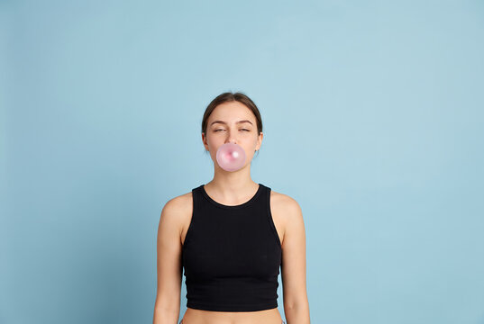Young woman blowing pink bubble gum against blue background