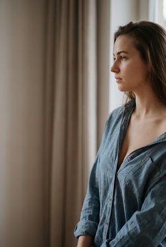 Young woman in denim shirt gazing out window thoughtfully