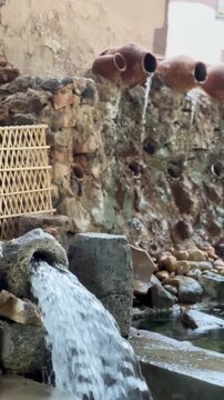 Rustic stone well and water cascading from clay pots in a traditional Arabic village.