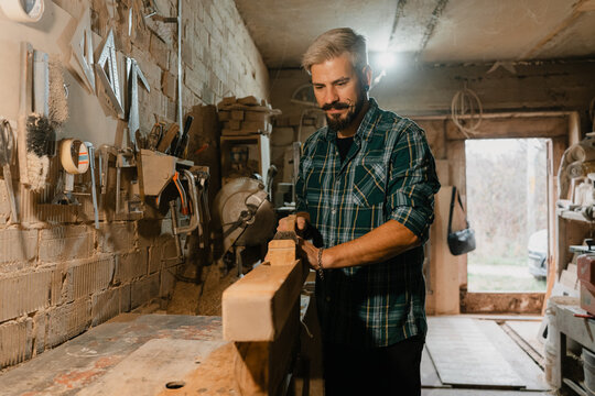 Carpenter planing wooden beam in rustic workshop, focused male craftsman working with tools