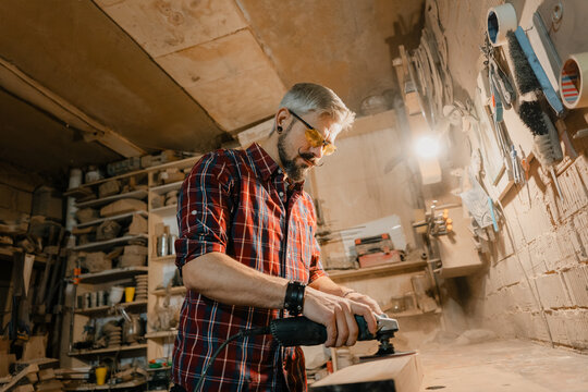 Carpenter sanding wood in a cluttered workshop creating handcrafted furniture with power tools