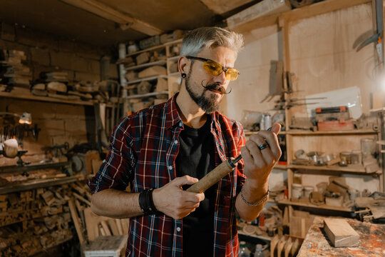 Experienced woodworker inspecting chisel blade in rustic woodworking workshop with focused expression