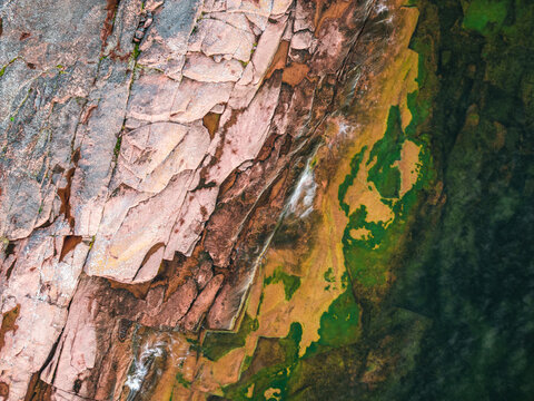 Aerial view of the rugged rocky coastline with layered stone formations, mossy textures, and clear water meeting the shore, Ulvohamn, Vasternorrland County, Sweden.
