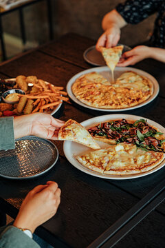 Diners share assorted pizzas, fries, fried snacks and refreshing mint drinks around a wooden restaurant table