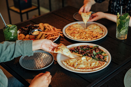 Diners share assorted pizzas, fries, fried snacks and refreshing mint drinks around a wooden restaurant table