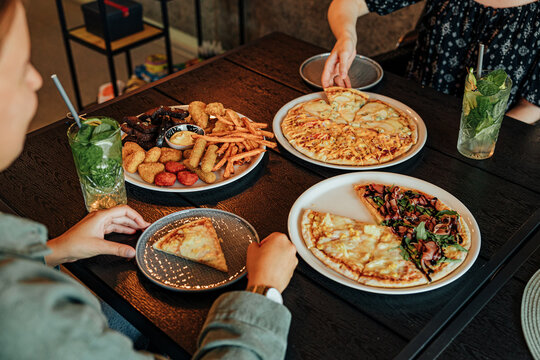 Diners share assorted pizzas, fries, fried snacks and refreshing mint drinks around a wooden restaurant table