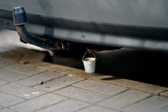 Tiny miniature metal bucket hanging as humorous accessory beneath rear bumper of grey car near tow hitch. Popular decorative accessory and good luck charm, miniature symbolic custom. Selective focus