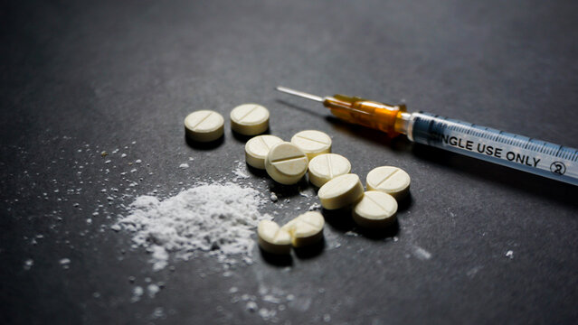 Disposable syringe and some pills on black background. Illegal drugs concept. 