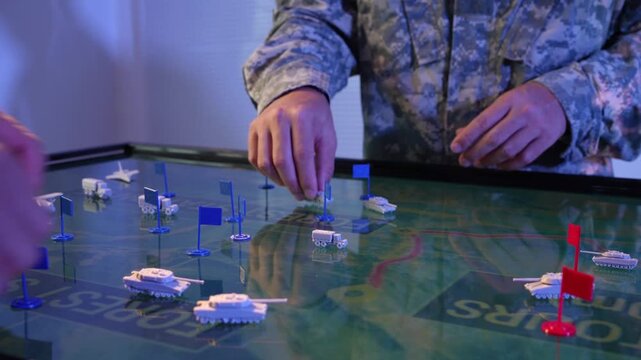 Soldiers in camouflage uniforms move miniature vehicles and markers on a tabletop map during a military strategy training exercise.
